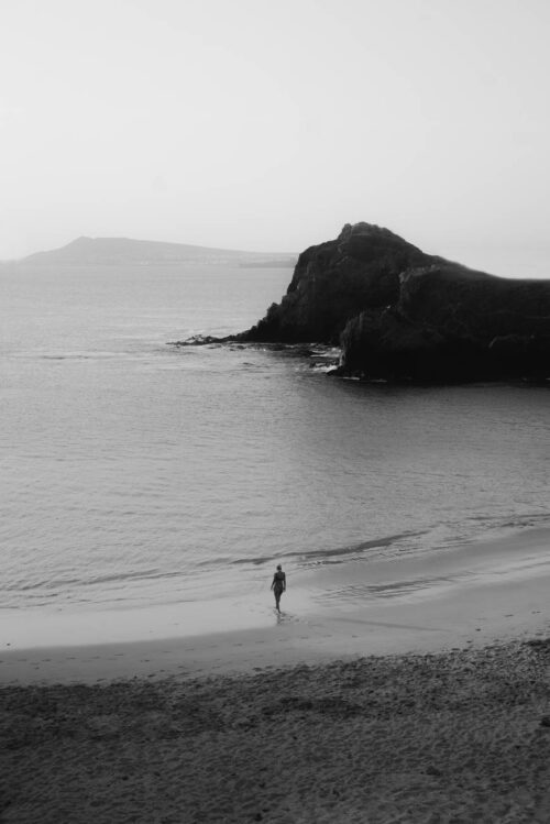 grayscale photo of person walking on beach